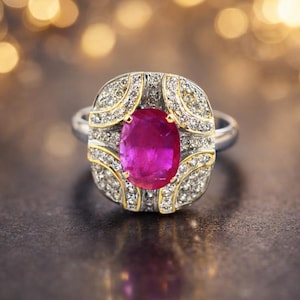 Könnte beinhalten: Ein silberner Ring mit einem großen, ovalen, leuchtend rosa Edelstein in der Mitte. Der Edelstein ist von kleineren, klaren Edelsteinen und goldenen Akzenten umgeben. Der Ring ist vor einem dunklen Hintergrund mit verschwommenen goldenen Lichtern platziert.