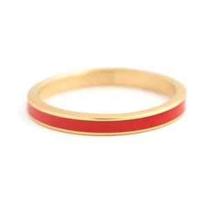 Puede incluir: Un anillo dorado con una banda de esmalte rojo vibrante. El anillo se presenta sobre un fondo blanco, resaltando su diseño simple pero elegante. Esta joya es adecuada para el uso diario.
