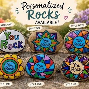 May include: Six smooth, oval-shaped stones painted with colourful designs and the text "You Rock". Style one is white with colourful letters. Styles two through six feature intricate geometric, floral, and mosaic patterns in vibrant colours.