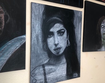 May include: A black and white chalk drawing of a woman with dark hair and a heart tattoo on her shoulder. The drawing is on a canvas and is framed. The artist's signature is in the bottom right corner.