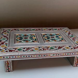 May include: A silver-coloured, decorative tray with a raised border and intricate floral designs in red, green, yellow, and blue. The tray has four legs and is made of metal.