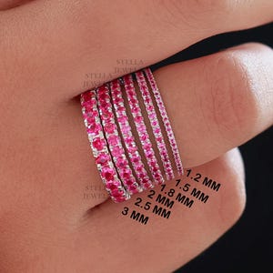 Könnte beinhalten: Ein Set aus sechs Ewigkeitsringen mit rosafarbenen Edelsteinen, jeder Ring hat eine andere Breite, beginnend bei 1,2 mm und ansteigend auf 3 mm. Die Ringe sind auf einer Hand gestapelt, wodurch der Größenunterschied deutlich wird.