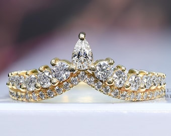 May include: A gold band ring with a pear-shaped diamond in the center and smaller round diamonds surrounding it. The ring is designed in a crown shape.