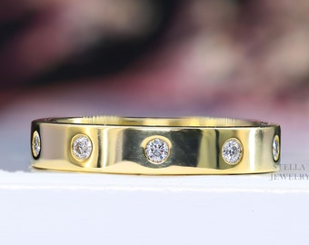 May include: A gold band ring with five small round clear stones set into the band. The ring is on a white surface with a blurred background.