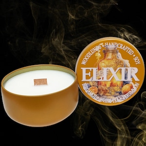 May include: A soy wax candle in a gold-colored tin with a wooden wick. The candle's lid is off, revealing the text "ELIXIR" and the words "Bergamot, White Tea, Persimmon". The candle is handcrafted.