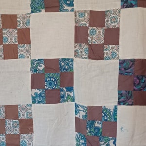 Könnte beinhalten: Eine Steppdecke mit Patchwork-Muster aus braunen, weißen und blauen Quadraten mit Blumenmustern. Die Steppdecke besteht aus Stoffquadraten, die zusammengenäht wurden, um ein größeres Muster zu erzeugen.