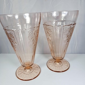 May include: Two pink glass goblets with a floral design and a fluted base.