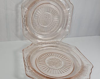 Puede incluir: Dos platos de vidrio rosa con un diseño floral y un borde festoneado.