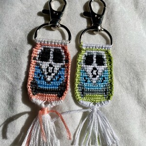 Puede incluir: Dos llaveros con forma de calavera con borlas. Un llavero es rosa y verde, el otro es verde y azul claro.