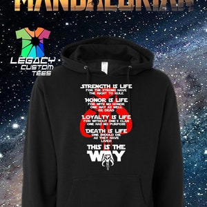 Op de afbeelding: Zwart hoodie met een witte grafische print van het Mandalorian-symbool en de tekst "This is the Way". De grafiek bevat ook de woorden "Strength is life", "Honor is life", "Loyalty is life" en "Death is life".