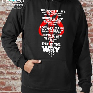 May include: Black hooded sweatshirt with a white graphic print of a Mandalorian symbol and the text "Strength is life for the strong have the right to rule. Honor is life for with no honor one may as well be dead. Loyalty is life for without one's clan one has no purpose. Death is life one should die as they have lived. This is the way."