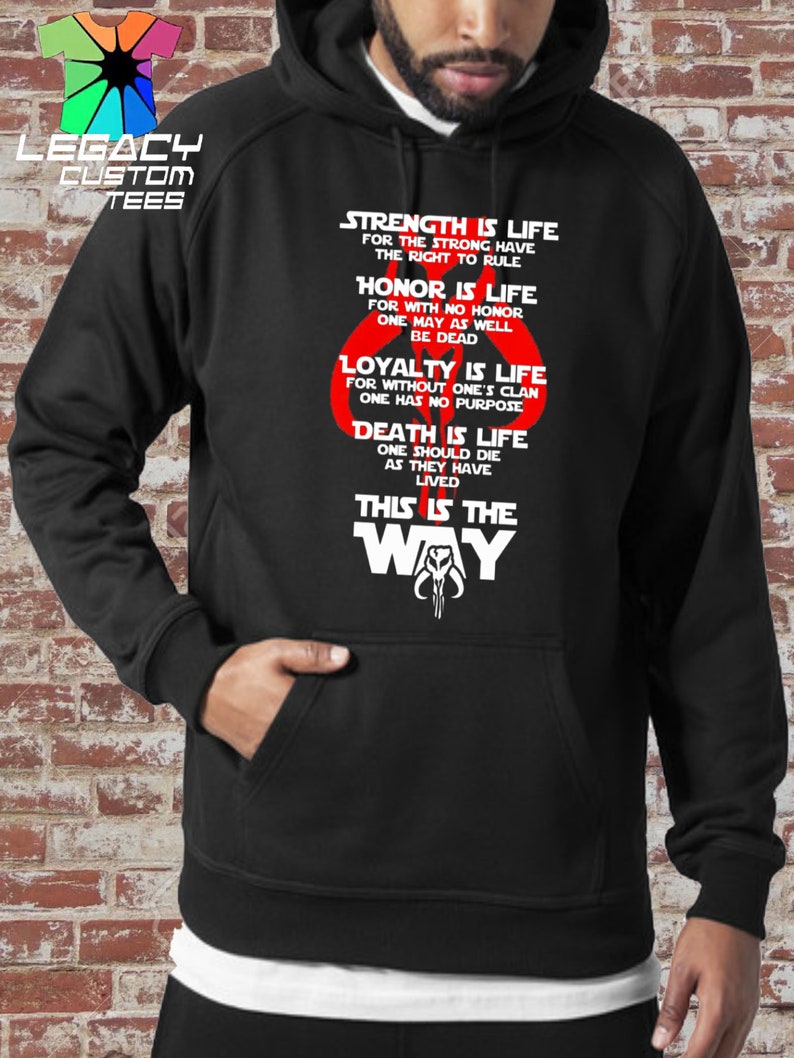 May include: Black hooded sweatshirt with a white graphic print of a Mandalorian symbol and the text "Strength is life for the strong have the right to rule. Honor is life for with no honor one may as well be dead. Loyalty is life for without one's clan one has no purpose. Death is life one should die as they have lived. This is the way."
