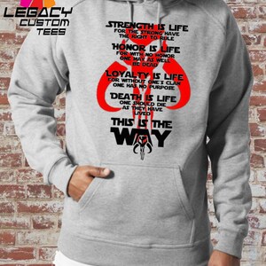 May include: A gray hooded sweatshirt with a black and red graphic print. The graphic features a Mandalorian symbol and text that reads "Strength is life for the strong have the right to rule. Honor is life for with no honor one may as well be dead. Loyalty is life for without one's clan one has no purpose. Death is life one should die as they have lived. This is the way."