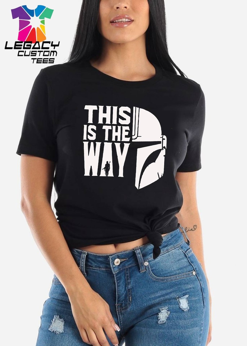 Puede incluir: Camiseta negra con un gr&aacute;fico blanco de un casco mandaloriano y el texto "This is the way".