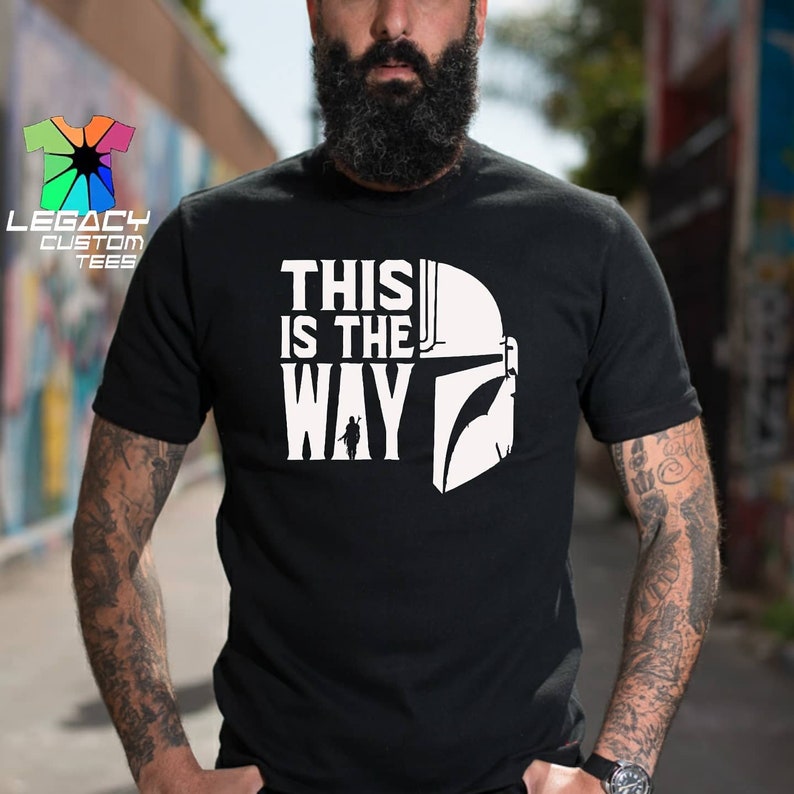 Puede incluir: Camiseta negra con un gr&aacute;fico blanco de un casco mandaloriano y el texto "This is the Way".