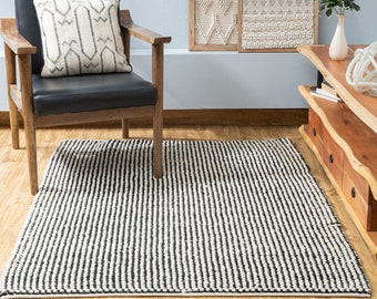 May include: Black and white striped rug with a black leather armchair and a white throw pillow with a geometric pattern. The rug is made of a thick, textured material.