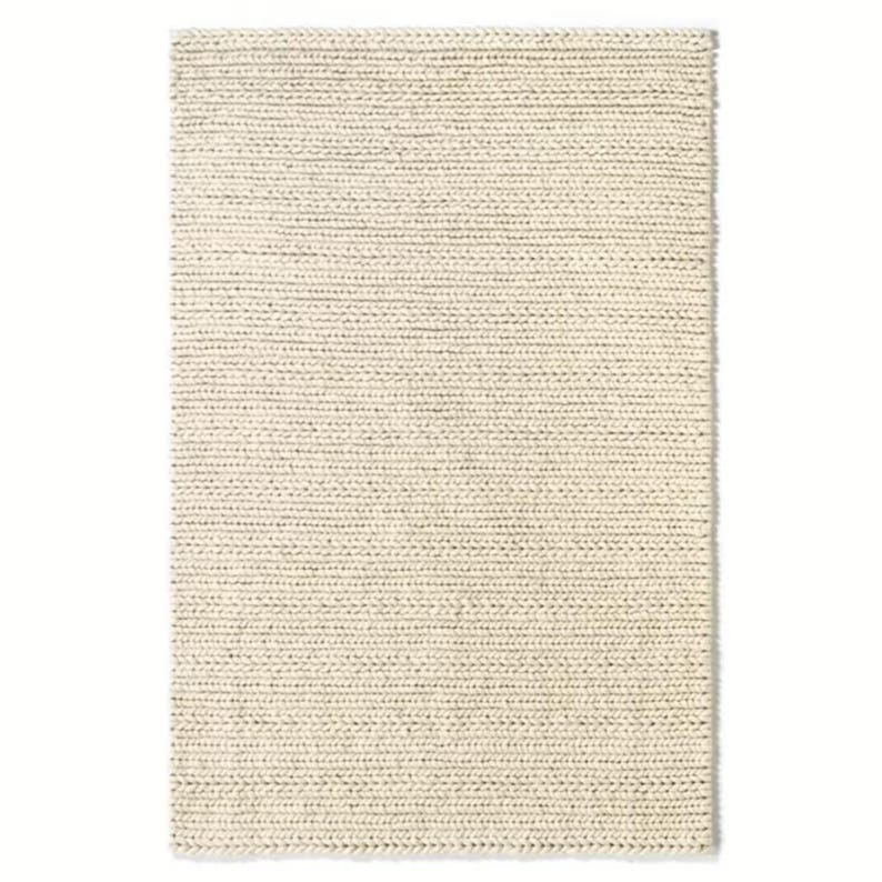 Puede incluir: Una alfombra blanca tejida con una textura sutil. La alfombra tiene forma rectangular y est&aacute; hecha de fibras naturales.