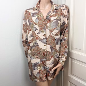 Könnte beinhalten: Ein langärmliges Button-Down-Hemd mit einem farbenfrohen Paisley- und Animal-Print-Muster. Das Hemd hat einen Kragen und eine Knopfleiste. Die Farbpalette umfasst Brauntöne, Beige und Burgunder.