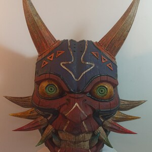 May include: A hand-painted wooden mask with a red, orange, and yellow color scheme. The mask has a fierce expression with large, green eyes and sharp teeth. The mask is decorated with intricate details, including a blue and white pattern on the forehead.
