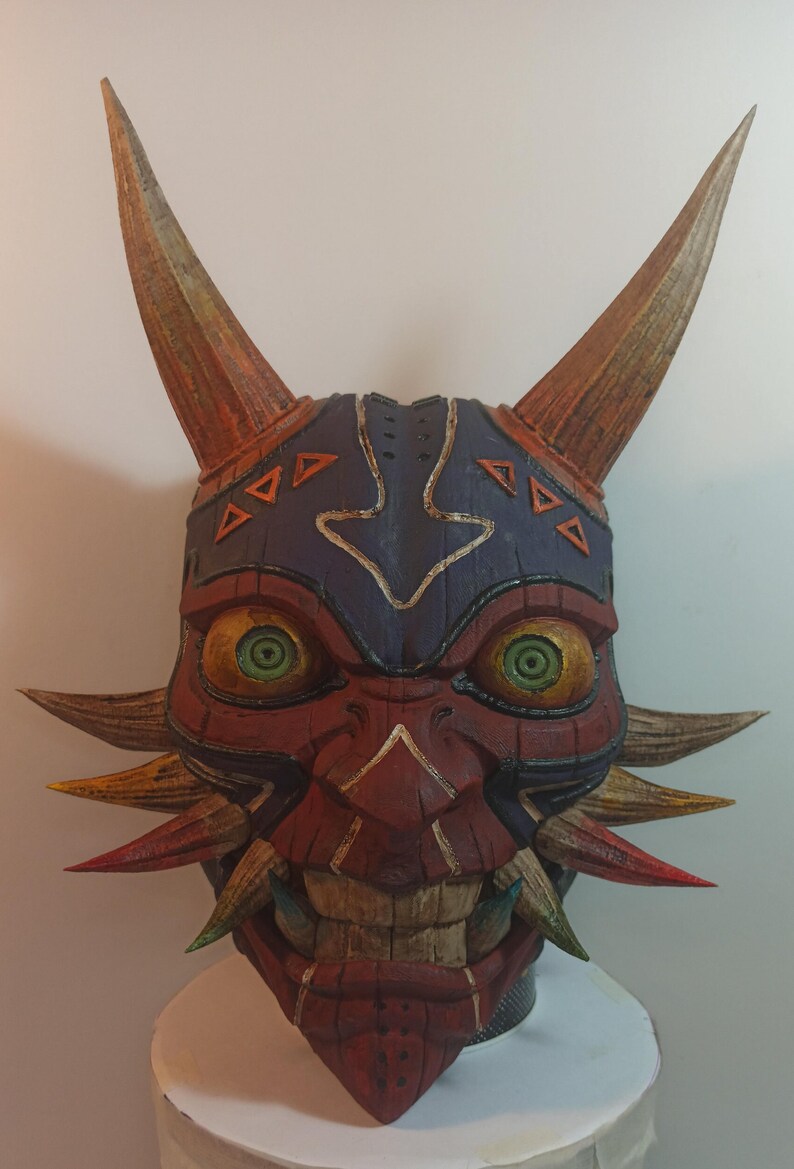 May include: A hand-painted wooden mask with a red, orange, and yellow color scheme. The mask has a fierce expression with large, green eyes and sharp teeth. The mask is decorated with intricate details, including a blue and white pattern on the forehead.