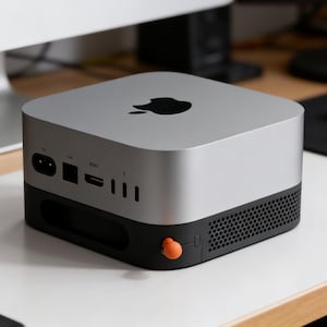 Può includere: Un computer Apple Mac Mini argento e nero. Il dispositivo ha un design quadrato con angoli arrotondati, un logo Apple nero sulla parte superiore e varie porte sul retro. Un pulsante di accensione arancione è visibile sulla parte anteriore.