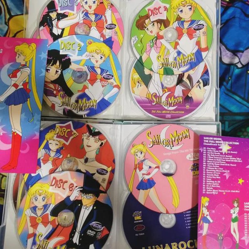 May include: A set of eight DVDs featuring the anime series Sailor Moon. The DVDs are in clear plastic cases with colorful artwork featuring the characters from the show. The cases are arranged in a row, with the titles "Sailor Moon" and "The Full Moon Collection" visible.