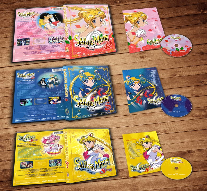 May include: A set of six DVD cases for the Sailor Moon anime series. The cases are blue, yellow, and pink with images of the characters from the show. The text on the cases reads "Sailor Moon R The Movie", "Sailor Moon S The Movie", and "Sailor Moon Super S The Movie".