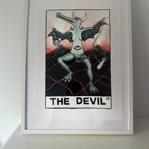 Puede incluir: Una ilustración en blanco y negro de una carta de tarot que representa una criatura con alas, cola y cuerpo humanoide. La carta está titulada "THE DEVIL" con el número "15" en la esquina.