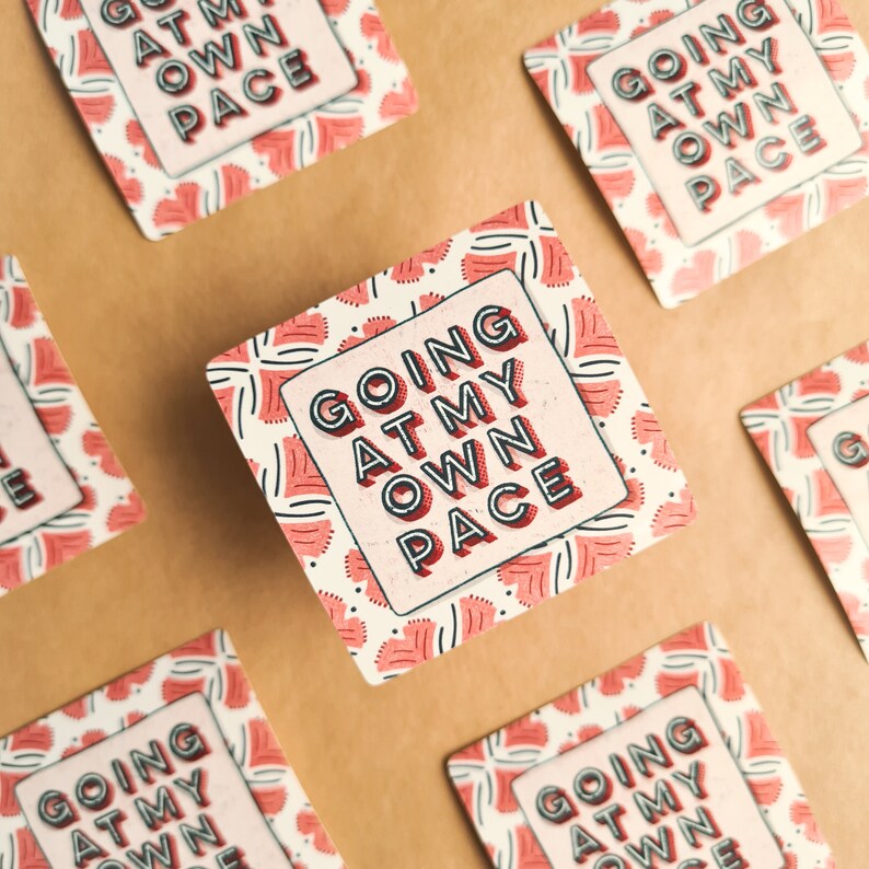 A glossy square shaped sticker with lettering saying "going at my own pace" in all caps