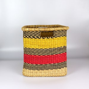 May include: A woven storage basket with black, yellow and red stripes. The basket is made from natural materials and has a rectangular shape.