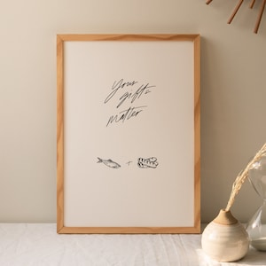 May include: A framed print with the text "Your gifts matter" in black cursive script. The print also features a black and white illustration of a fish and a loaf of bread.