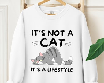 以下が含まれることがあります： グレーの猫のイラストと「猫じゃない、ライフスタイルなんだ。」というテキストが入った白いスウェットシャツ