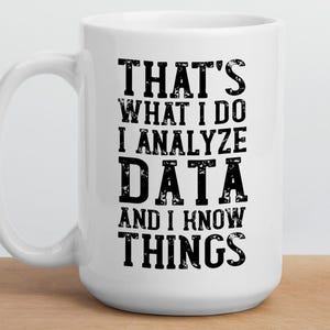Op de afbeelding: Een witte keramische mok met zwarte tekst in een verweerde stijl die luidt: THAT'S WHAT I DO I ANALYZE DATA AND I KNOW THINGS. De mok heeft een gebogen handvat aan de linkerkant en een gladde afwerking. Rechtsboven staat het logo DECKSY DESIGNS.