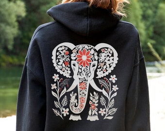 Puede incluir: Sudadera con capucha negra con un diseño de elefante floral blanco en la espalda. El elefante tiene flores rojas en su trompa y orejas. El texto "AVAILABLE IN MULTIPLE SIZES AND COLORS" está en la parte inferior de la imagen.