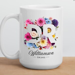 Puede incluir: Taza de cerámica blanca con un diseño floral que presenta las letras "DR" en blanco. El texto "Williamson - Est. 2025" está impreso debajo del diseño floral.