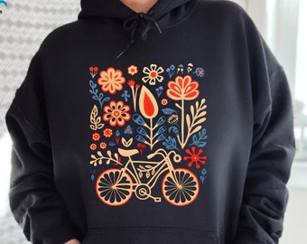 Puede incluir: Sudadera con capucha negra con un diseño floral colorido que incluye una bicicleta en el centro. El diseño incluye flores rojas, naranjas, amarillas, azules y verdes.