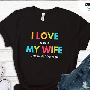 Pu&ograve; includere: T-shirt nero con la scritta "I LOVE it when MY WIFE lets me buy car parts" a lettere colorate. La maglietta &egrave; abbinata a jeans blu e scarpe da ginnastica bianche. La frase "AVAILABLE IN MULTIPLE CLOTHING OPTIONS" &egrave; in basso.