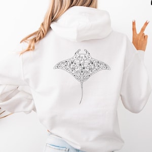 May include: White hoodie with a black and white manta ray design on the back, decorated with floral patterns. The text "AVAILABLE IN MULTIPLE SIZES AND COLOURS" is at the bottom. A casual, comfortable garment.