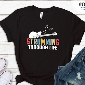 May include: Black t-shirt with a colorful graphic of a guitar and the text "Strumming Through Life".