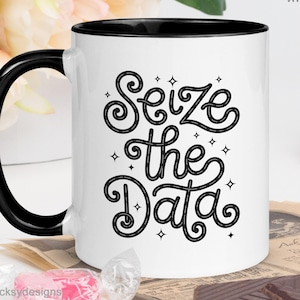 May include: White ceramic mug with a black interior and handle. The mug features the text "Seize the Data" in a black, stylized font with decorative star accents. The mug has the "DECKSY DESIGNS" logo.