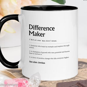 May include: White ceramic mug with a black interior and handle. The mug features the text "Difference Maker" with a definition. The mug is decorated with the text "PERSONALISE YOUR MUG" and "MORE COLOUR OPTIONS".