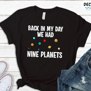 May include: Black t-shirt with white text that reads "Back in my day we had nine planets". The text is surrounded by small images of planets.