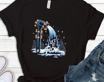 Pode incluir: Camiseta preta com um design de chave inglesa azul da qual flui água, adornada com luzes de corda. O texto "LET IT FLOW" é impresso em branco. O design é ambientado em uma cena de inverno nevada.