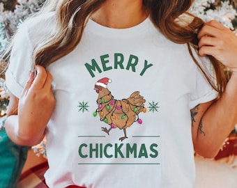 May include: White t-shirt with a green graphic of a chicken wearing a Santa hat and Christmas lights. The text "Merry Chickmas" is below the chicken.