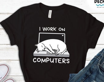 Op de afbeelding: Zwart T-shirt met een witte illustratie van een kat die op een laptop slaapt. De tekst "I work on computers" staat onder de afbeelding.