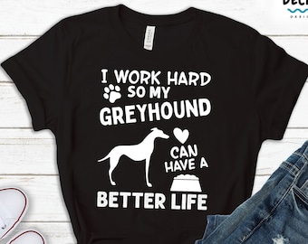 Könnte beinhalten: Schwarzes T-Shirt mit weißem Text, der lautet "Ich arbeite hart, damit mein Greyhound ein besseres Leben haben kann". Der Text wird von einem weißen Pfotenabdruck, einer weißen Silhouette eines Greyhounds, einem weißen Herzen und einer weißen Schüssel begleitet.