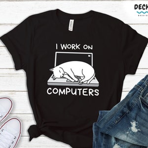 Puede incluir: Camiseta negra con una ilustración blanca de un gato durmiendo en un portátil. El texto "I work on computers" está impreso debajo de la imagen.