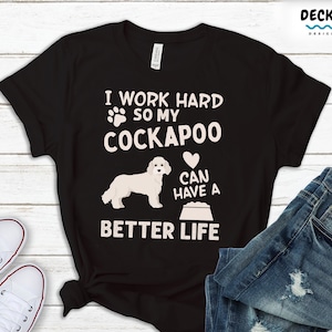 May include: Black t-shirt with a white graphic design featuring a Cockapoo dog and the text "I work hard so my Cockapoo can have a better life".