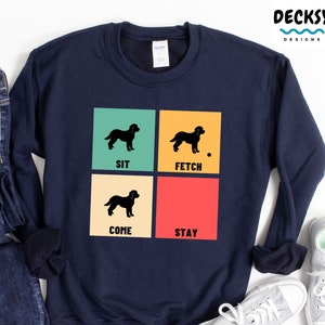 May include: A navy blue sweatshirt with a retro-style design featuring a black silhouette of a dog in four different poses. The poses are labelled "Sit", "Fetch", "Come", and "Stay".
