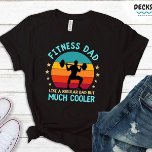 Puede incluir: Camiseta negra con un gr&aacute;fico retro de una persona levantando pesas. El gr&aacute;fico dice "Fitness Dad" y "Like a regular dad but much cooler".